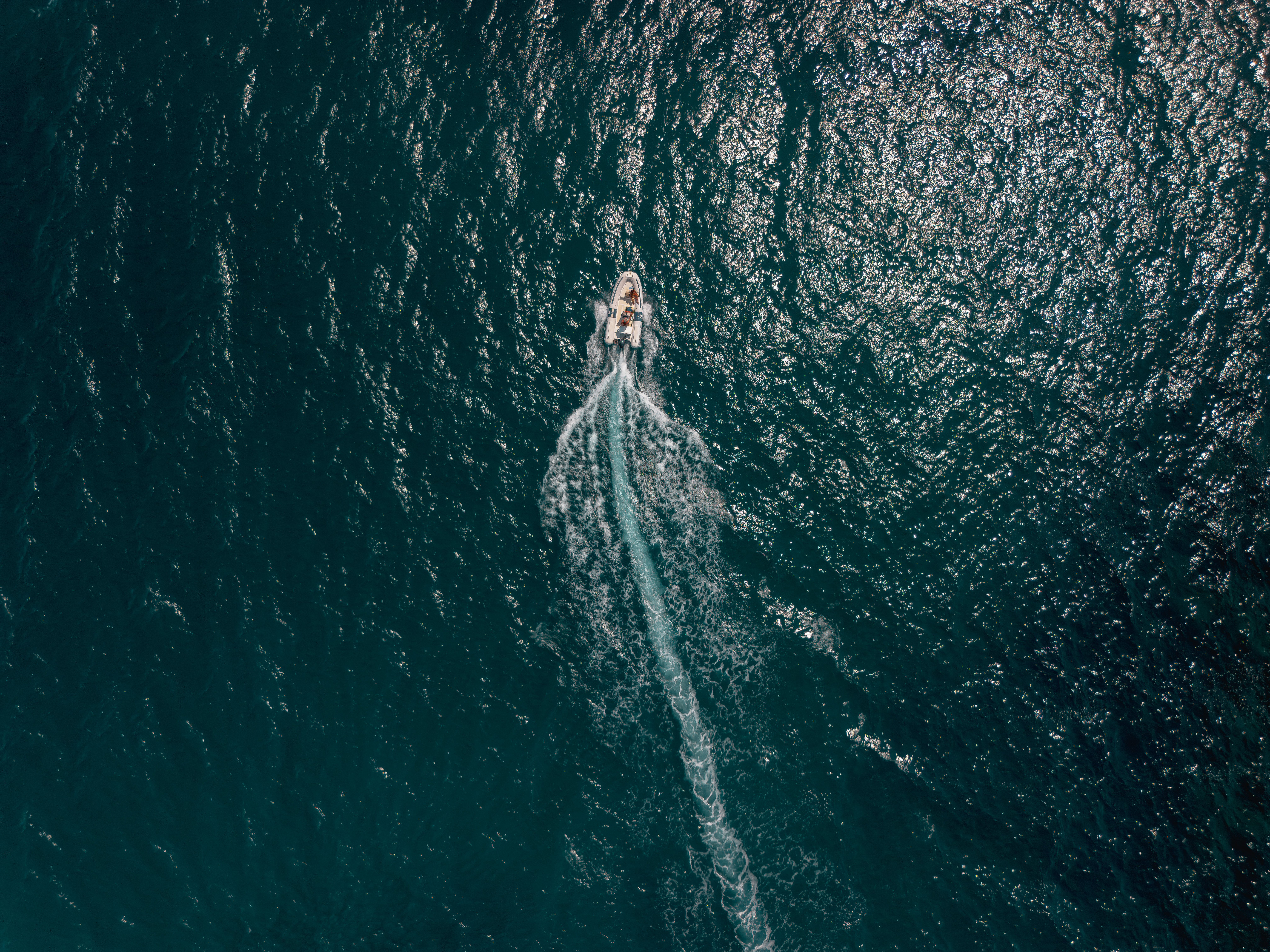 A speedboat cruising on the deep blue ocean, captured from above, creating a trail in the water.