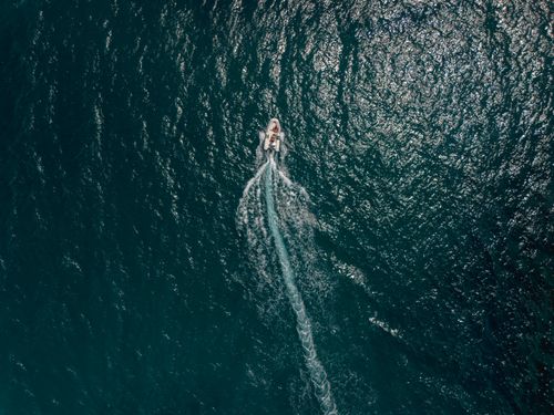 Free A speedboat cruising on the deep blue ocean, captured from above, creating a trail in the water. Stock Photo