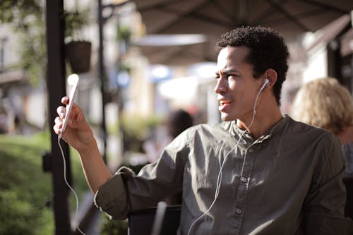 Free Side view of black male wearing summer shirt using smartphone for video chatting and sitting on outdoor terrace while communicating on social media Stock Photo