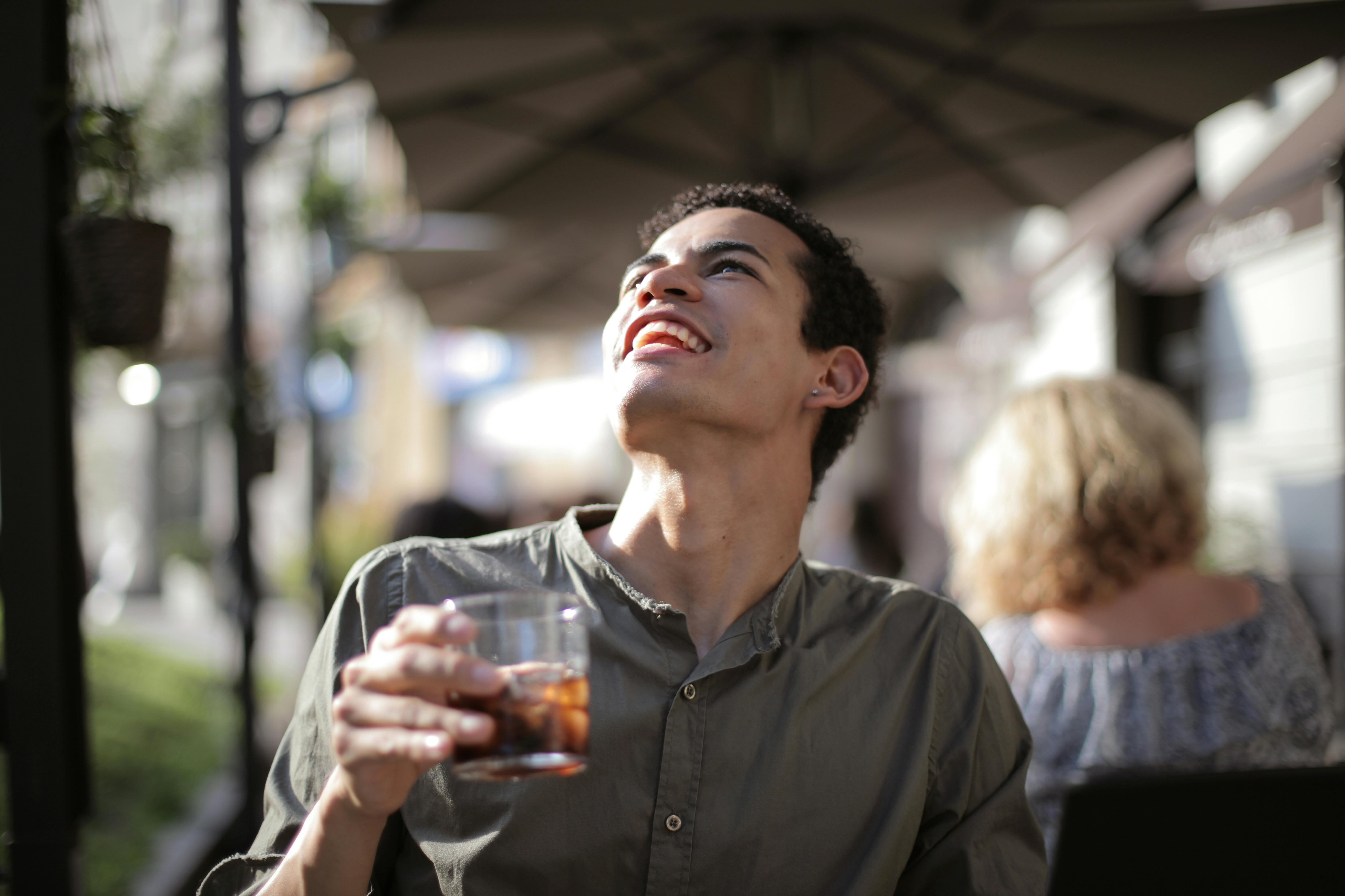 happy ethnic man having drink with ice cubes in street cafe in sunny hot day