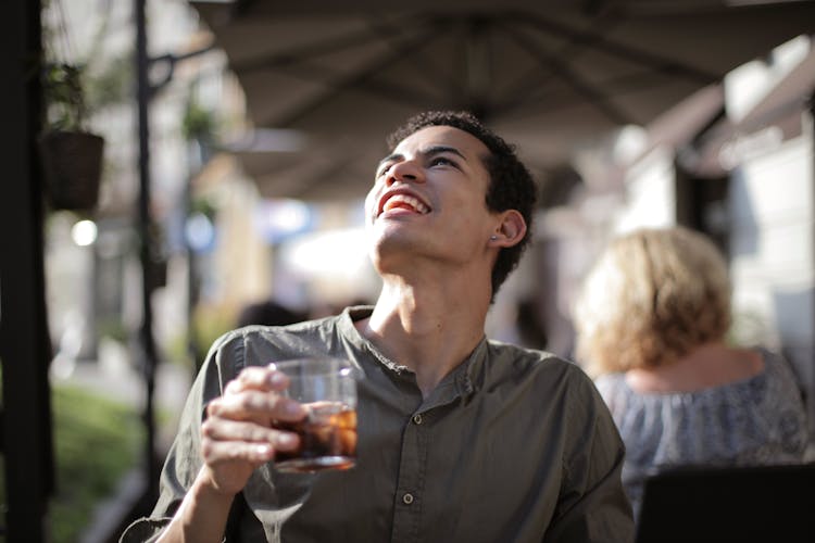 Happy Ethnic Man Having Drink With Ice Cubes In Street Cafe In Sunny Hot Day