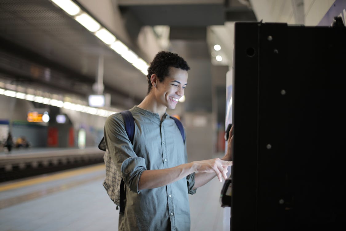 Hombre étnico alegre que usa una máquina expendedora de boletos en la estación de metro