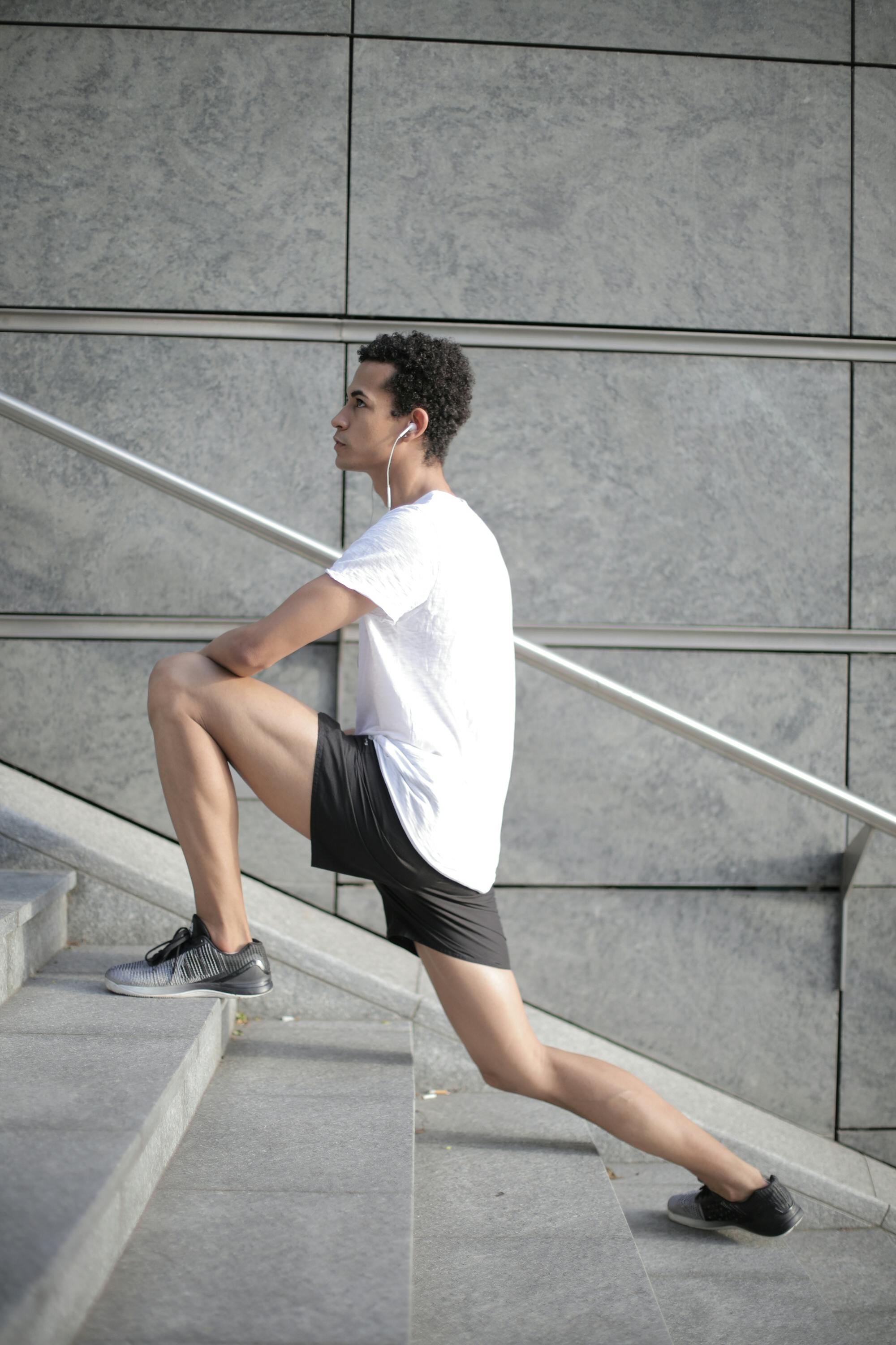 millennial ethnic male athlete stretching legs on stairs in city