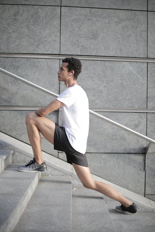 Free Millennial ethnic male athlete stretching legs on stairs in city Stock Photo