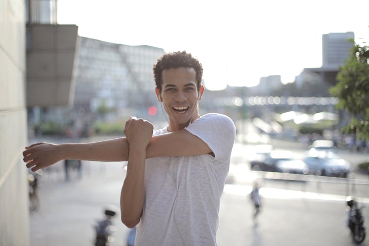 Happy Young Ethnic Sportsman Stretching Arms While Warming Up Before Training On Street In City