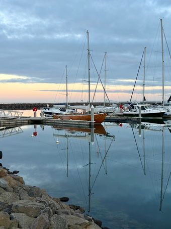 Moored yachts mirrored in a harbour at twilight. Photo: Joolsmagools on Pexels