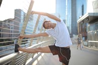 在阳光明媚的日子里，一位冷静专注的非洲裔美国男性运动员，穿着运动服、戴着耳机，闭着眼睛靠在金属围栏上，一边听音乐一边做侧弯伸展