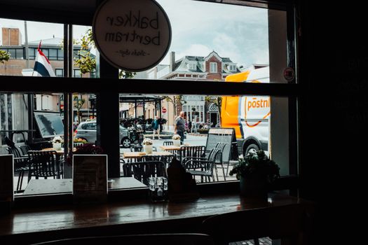 View from a cafe window featuring outdoor seating, street scene, and PostNL van in a Dutch city.