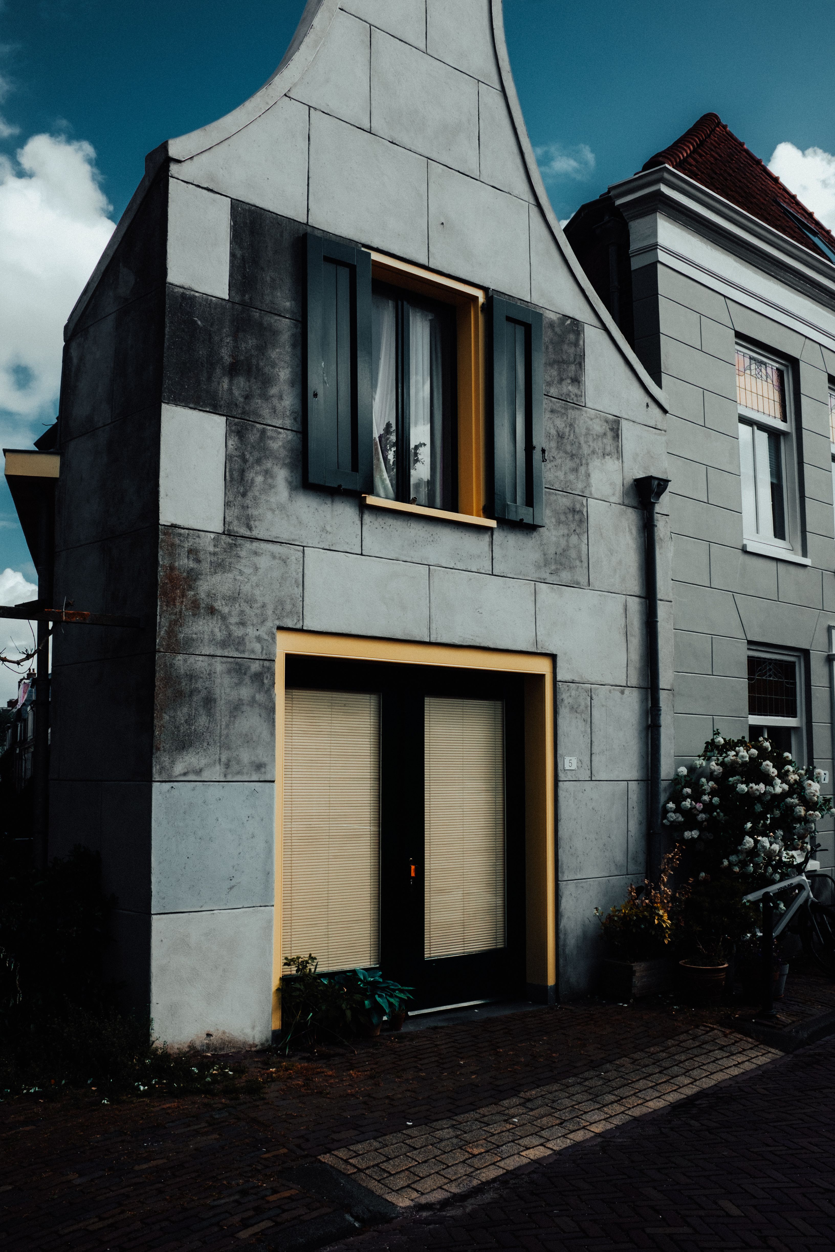 A vintage gray stucco house with unique architecture featuring yellow trim and lush floral accents.