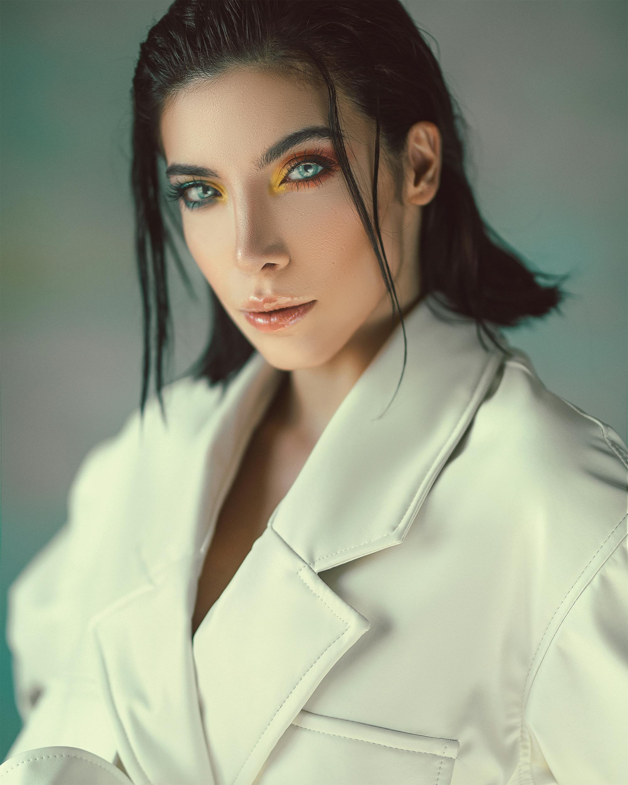 Stylish portrait of a woman with colorful eye makeup, wearing a white coat.