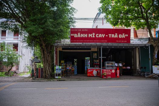 Street vendor shop in Hanoi selling Bánh Mì Cay and Trà Đá under a shady tree.