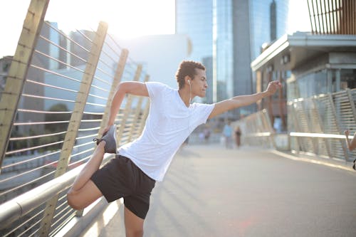 Free Young African American athlete in earbuds listening to music and stretching legs while training alone on street Stock Photo