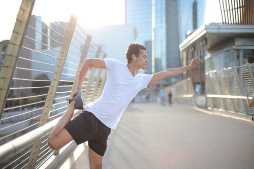 Free Determined ethnic sportsman in earphones sport clothes stretching legs while listening to music and training alone on street against blurred urban environment Stock Photo