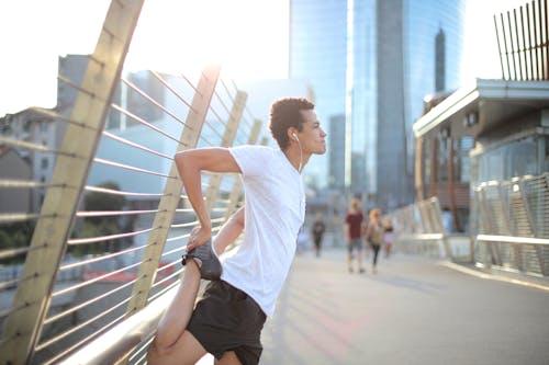 음악을 듣고 거리에서 달리기 전에 몸을 스트레칭하는 이어폰에 집중된 밀레 니얼 민족 운동 선수