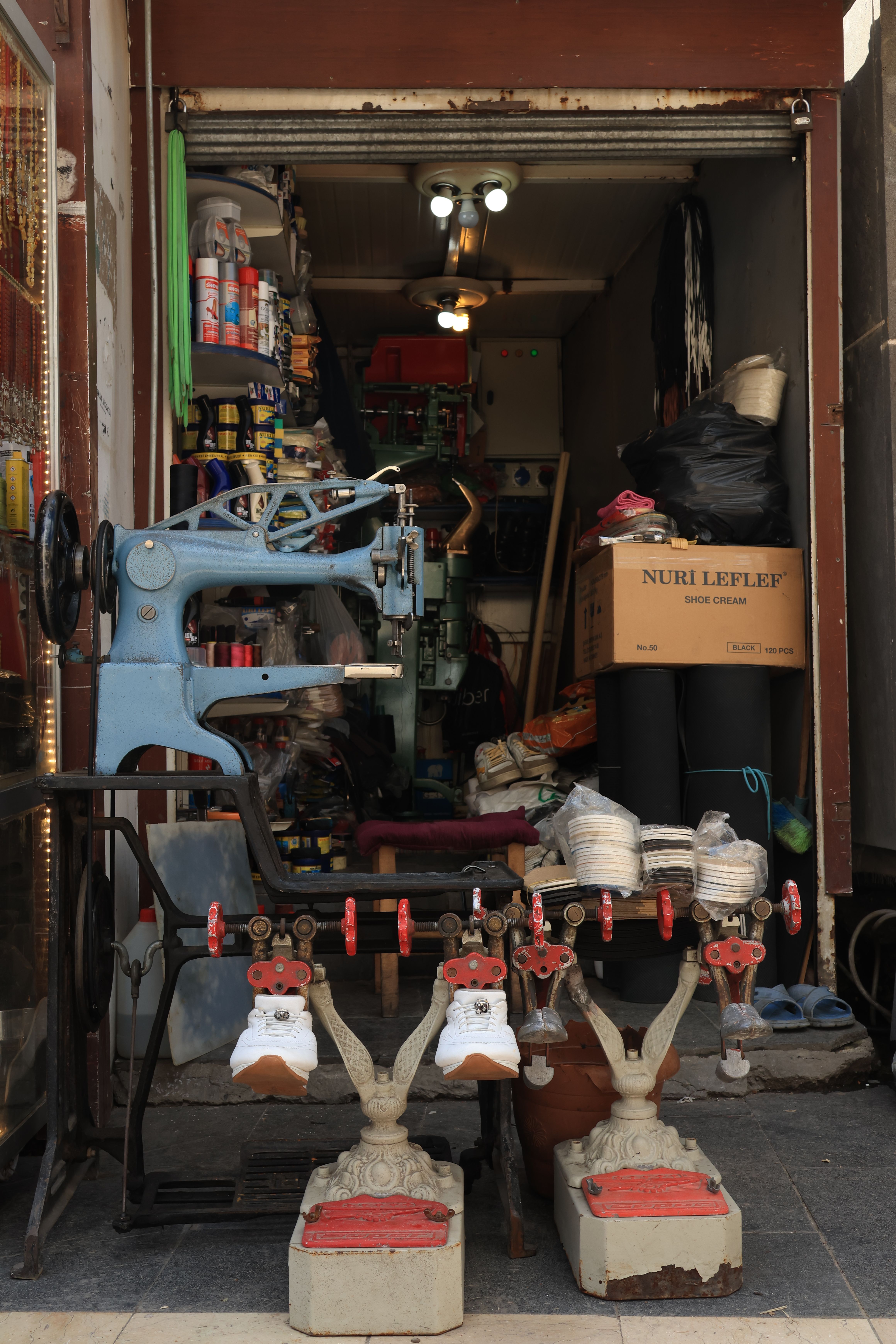 A small, cluttered shoe repair shop with vintage machinery and various supplies.