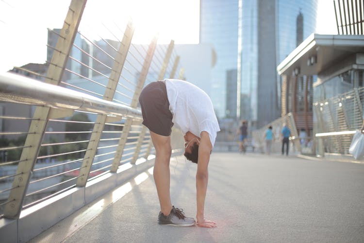 Flexible Ethnic Athlete Doing Standing Forward Bend Exercise On Street In City