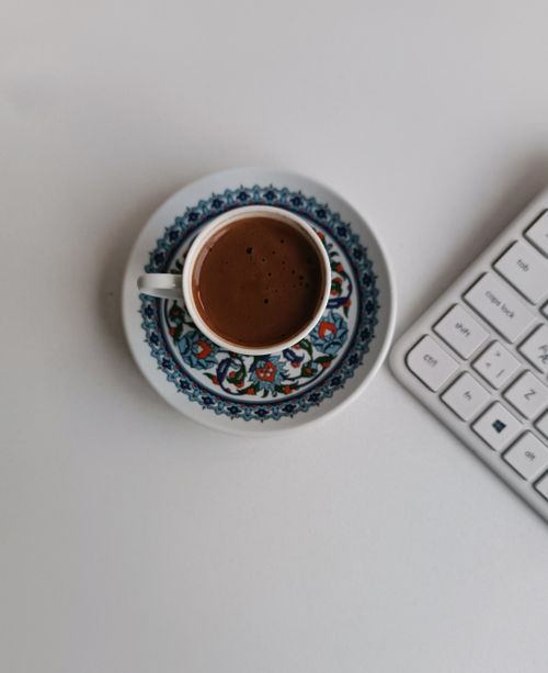 Free Ornate coffee cup with floral saucer beside keyboard on a workspace. Stock Photo