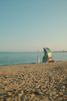 A peaceful beach scene featuring a calm ocean and a colorful advertising sail under a clear sky.