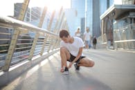 一位年轻的运动员在都市摩天大楼间的天桥上蹲下系鞋带，展现了积极的生活方式