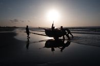 Fishermen push a boat into the sea at sunrise on Phan Thiet beach, Vietnam.
