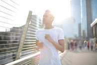 From below calm young African American sportsman in earphones and sportswear looking away with interest and contemplating while running alone along street and listening to music against blurred urb...