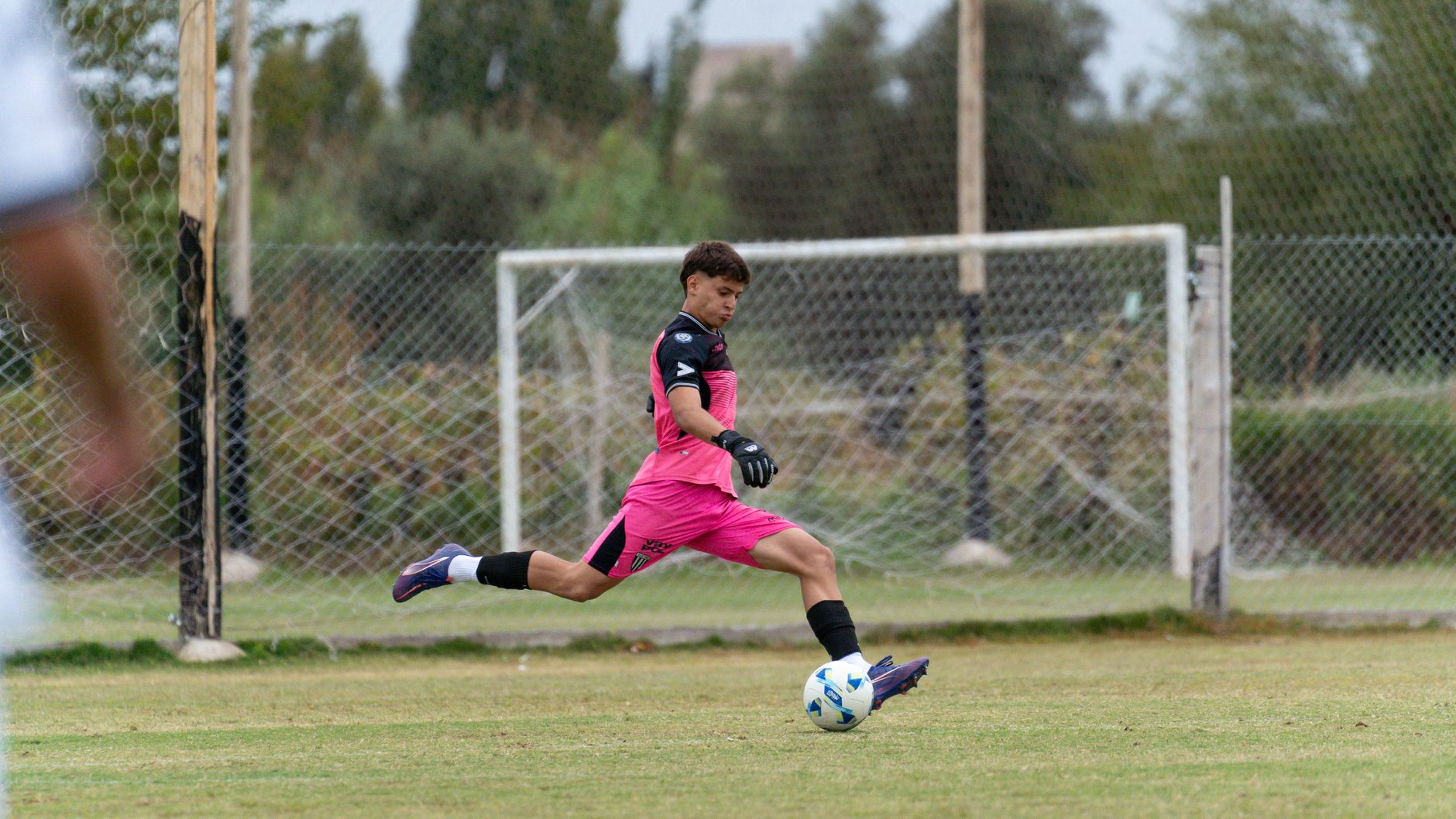a young footballer practising close control between orange cones on a quiet grass training pitch