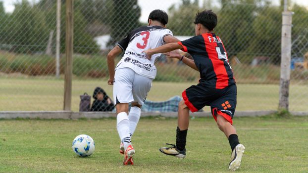 Two teenage boys competing in a soccer match on an outdoor field.