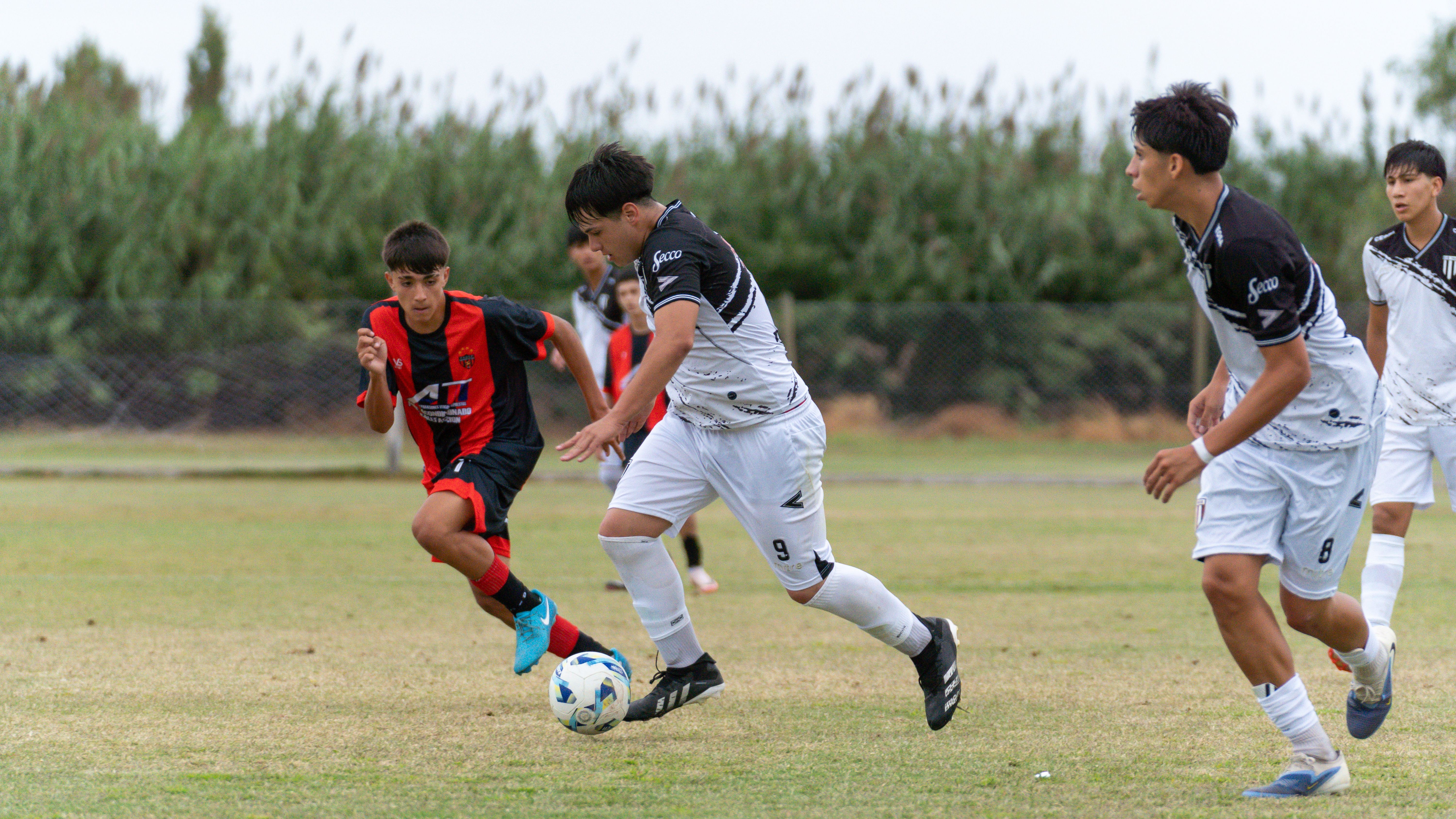 Dynamic action shot of teenagers playing soccer outdoors on a grassy field.