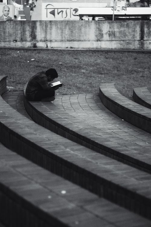 Free A black and white photo of a person reading on curved concrete steps outdoors. Stock Photo