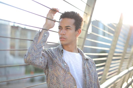 年轻男性站在桥上，手扶栏杆的水平铁丝，向远处望去