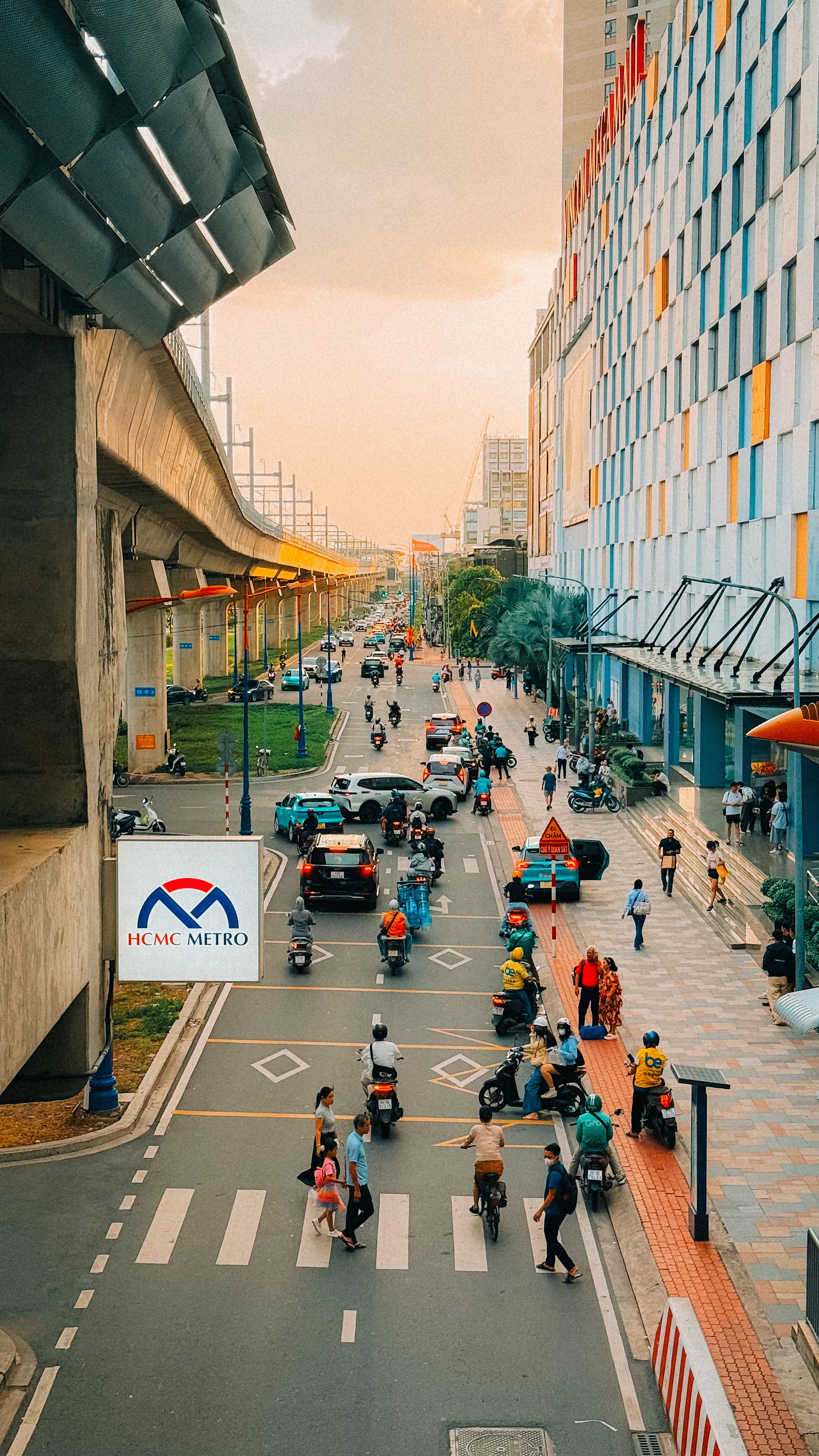 Vibrant street view of Ho Chi Minh City with motorcycles and pedestrians under the metro line.