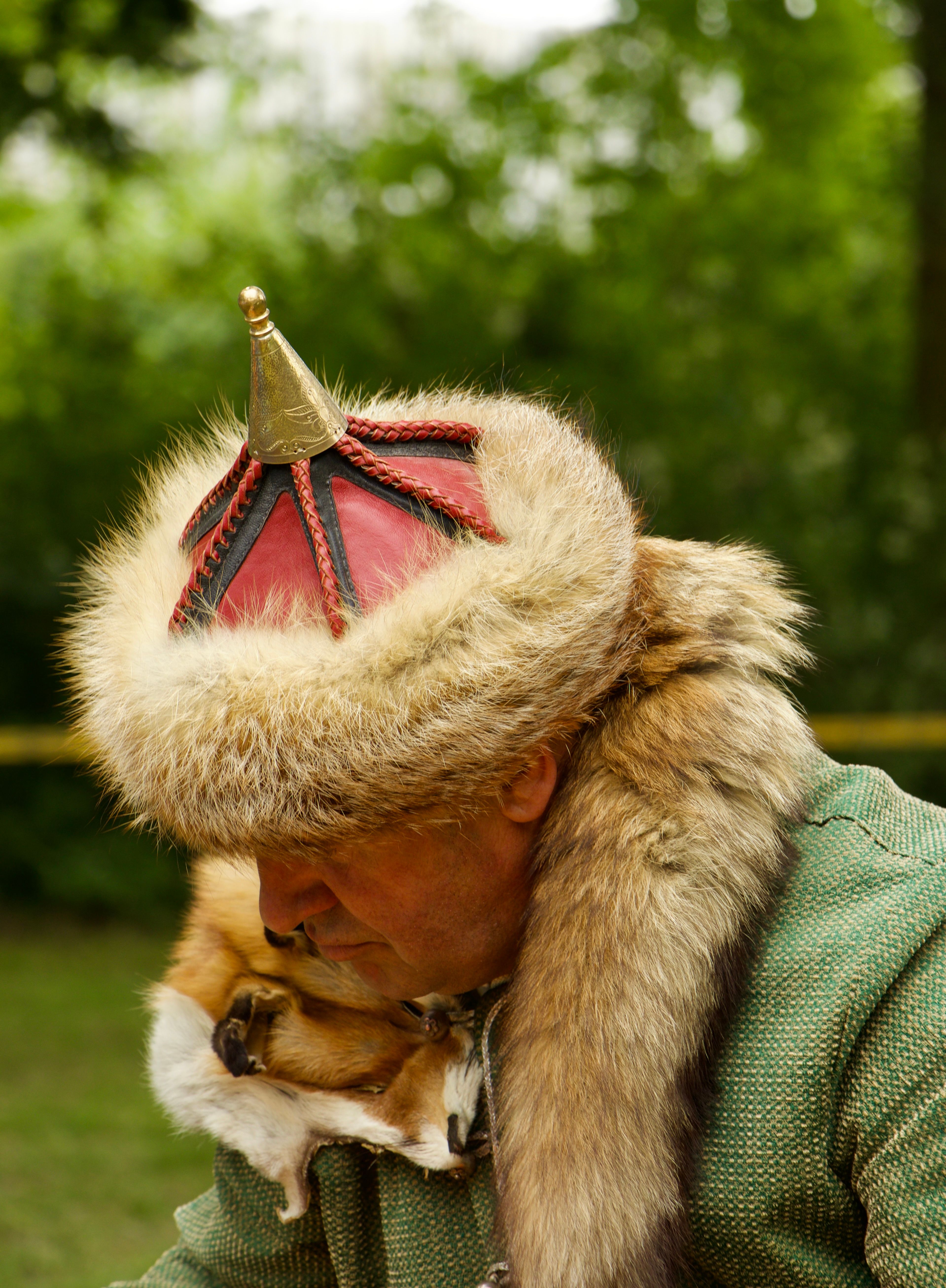 A person wearing a traditional fur hat with a historical costume in a natural setting.