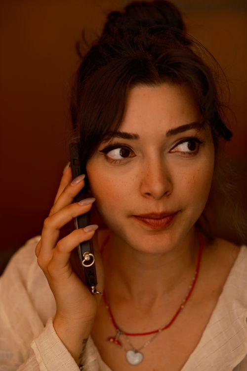 Free A woman with expressive eyes talks on a phone during a cozy indoor setting, creating a warm ambiance. Stock Photo