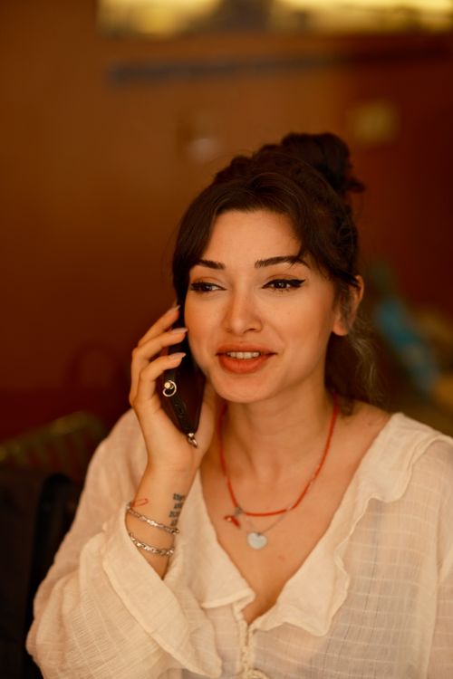 Free A cheerful woman chatting on her phone in an inviting, warm-toned indoor space. Stock Photo