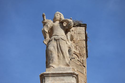 A detailed view of an ancient stone statue in El Puerto de Santa María, Spain, under a clear blue sky.