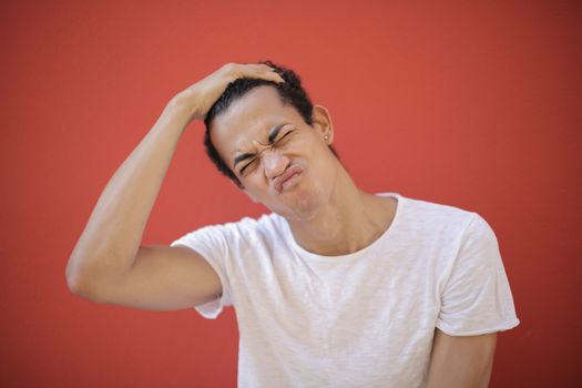 Happy ethnic with piercing putting hand on head and frowning face while standing against red background