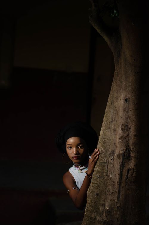 Free Stylish woman in Lagos peeks from behind a tree, showcasing grace and fashion. Stock Photo