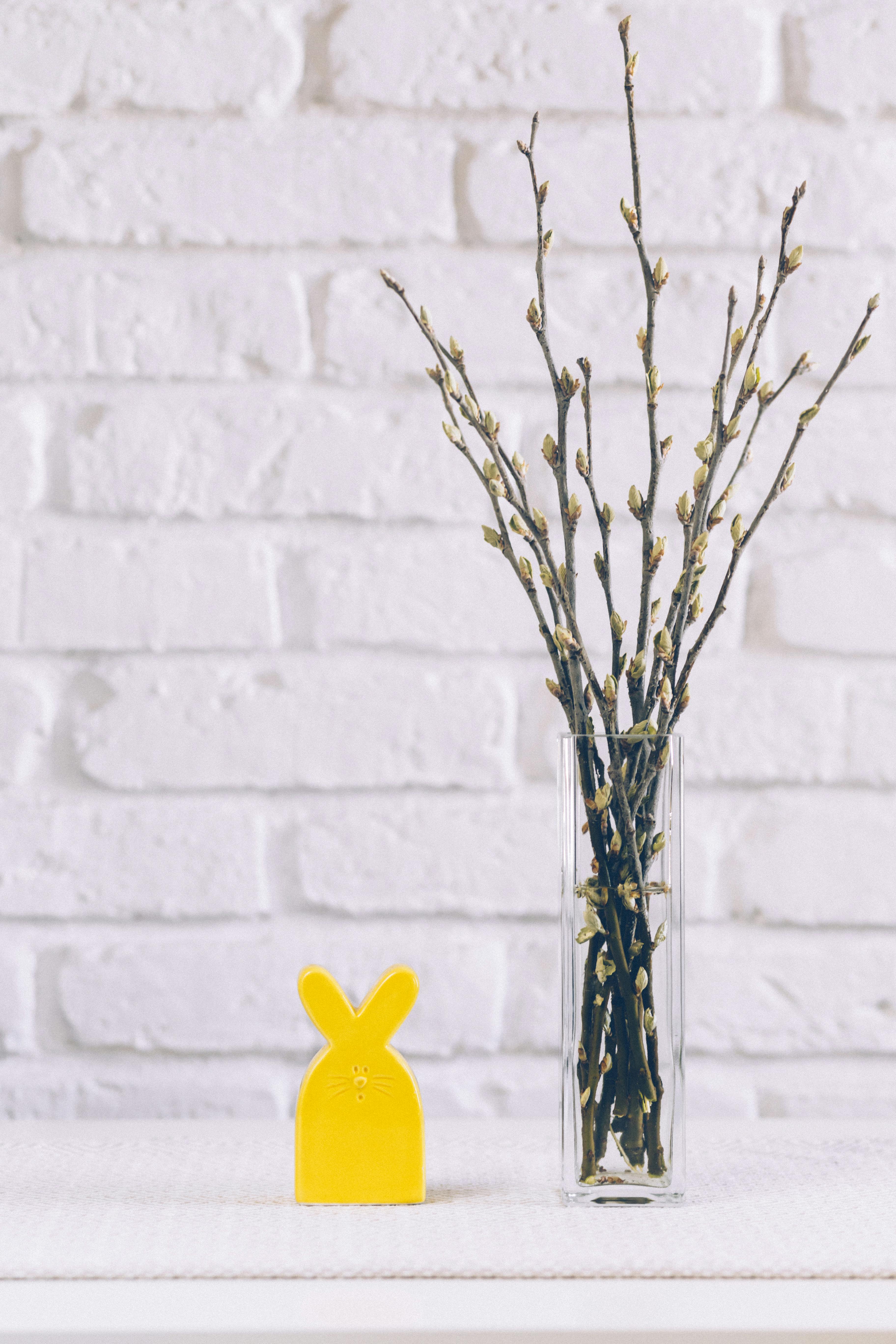 黄色复活节兔子和花瓶靠着白砖墙，旁边有树枝
