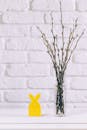 黄色复活节兔子和花瓶靠着白砖墙，旁边有树枝