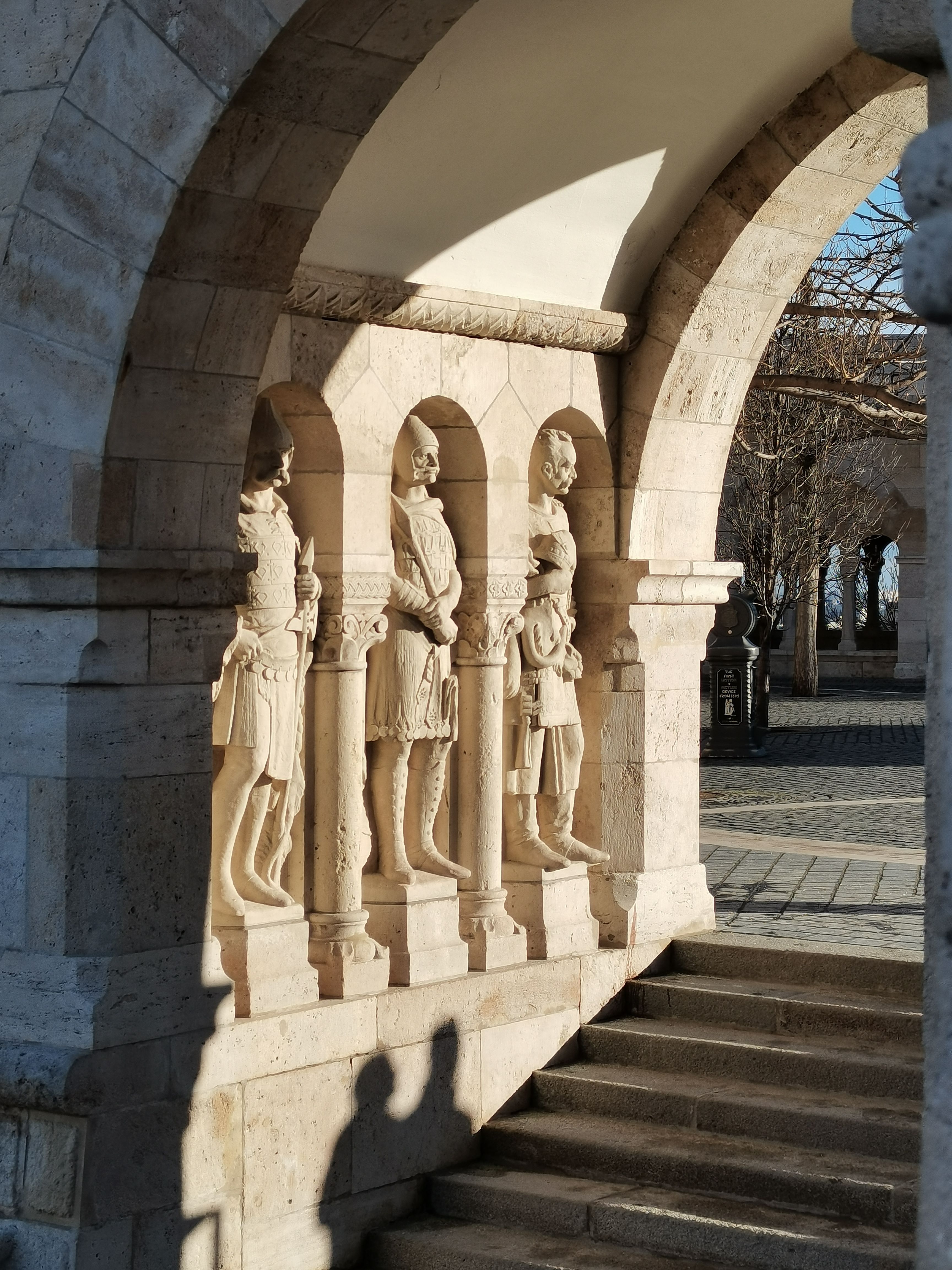 Stone statues at Fisherman's Bastion in Budapest, captured in early morning light, showcasing arches and shadow play.