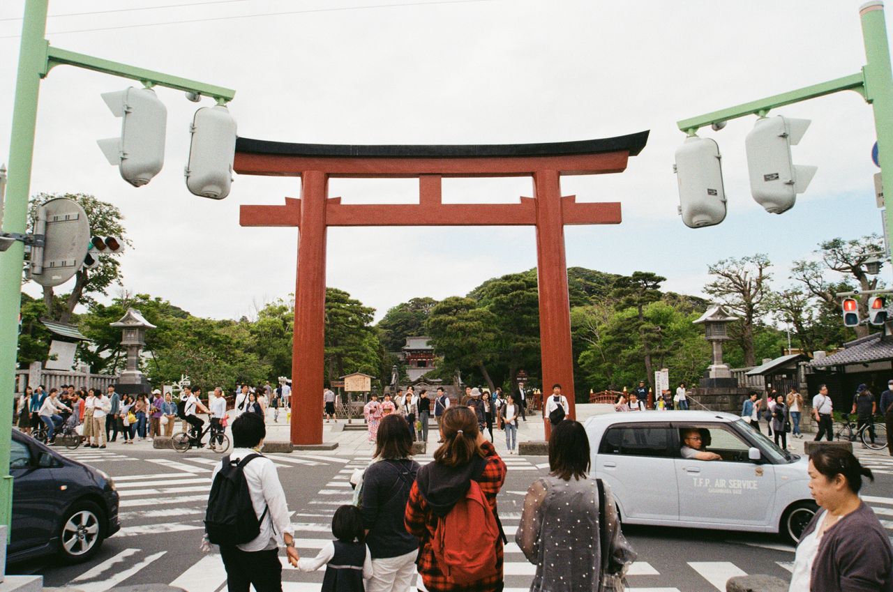 people crossing at a busy intersection under a large red torii gate in