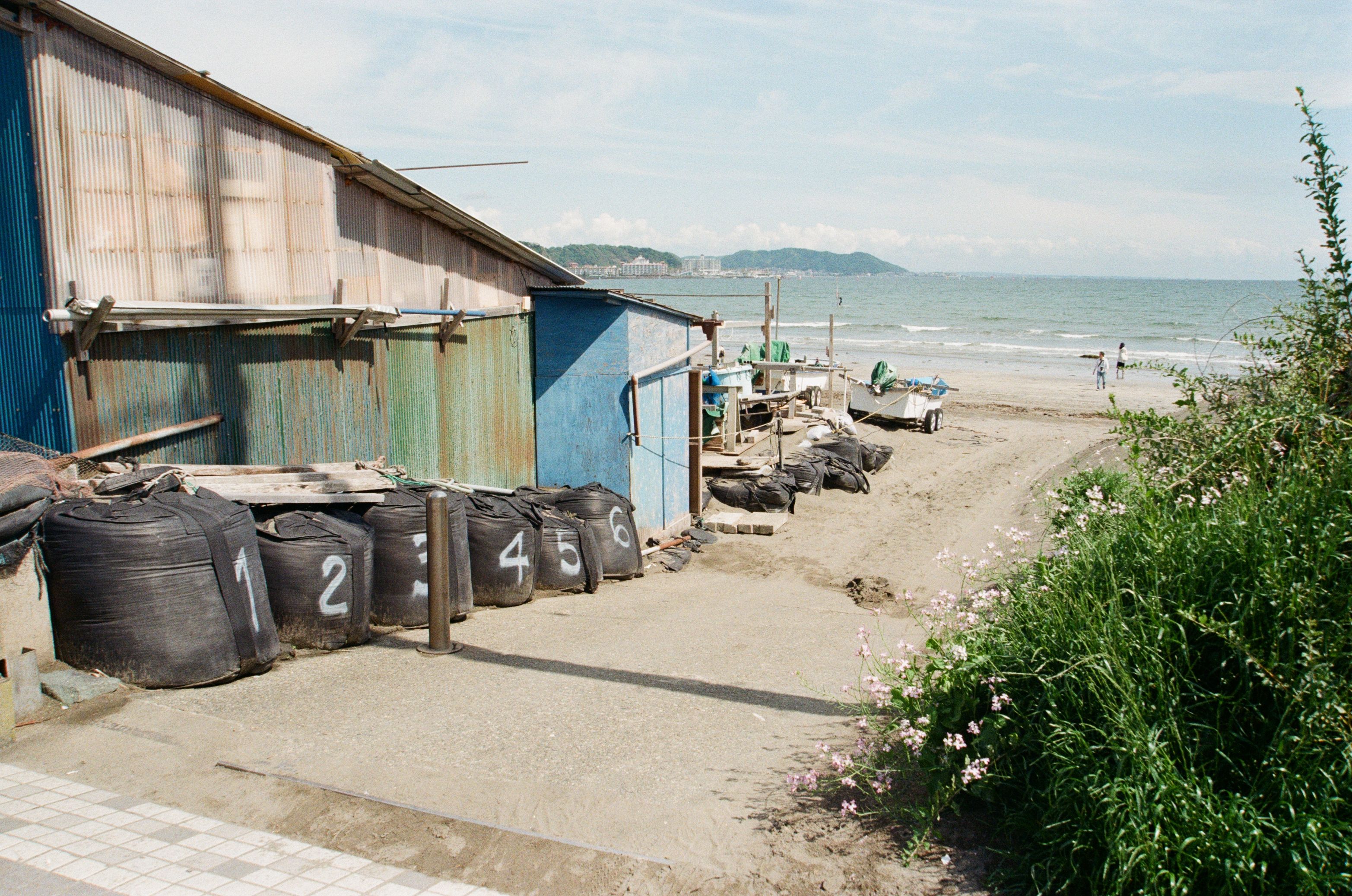 Coastal view of a rustic structure with numbered bags on Kamakura beach, Japan.