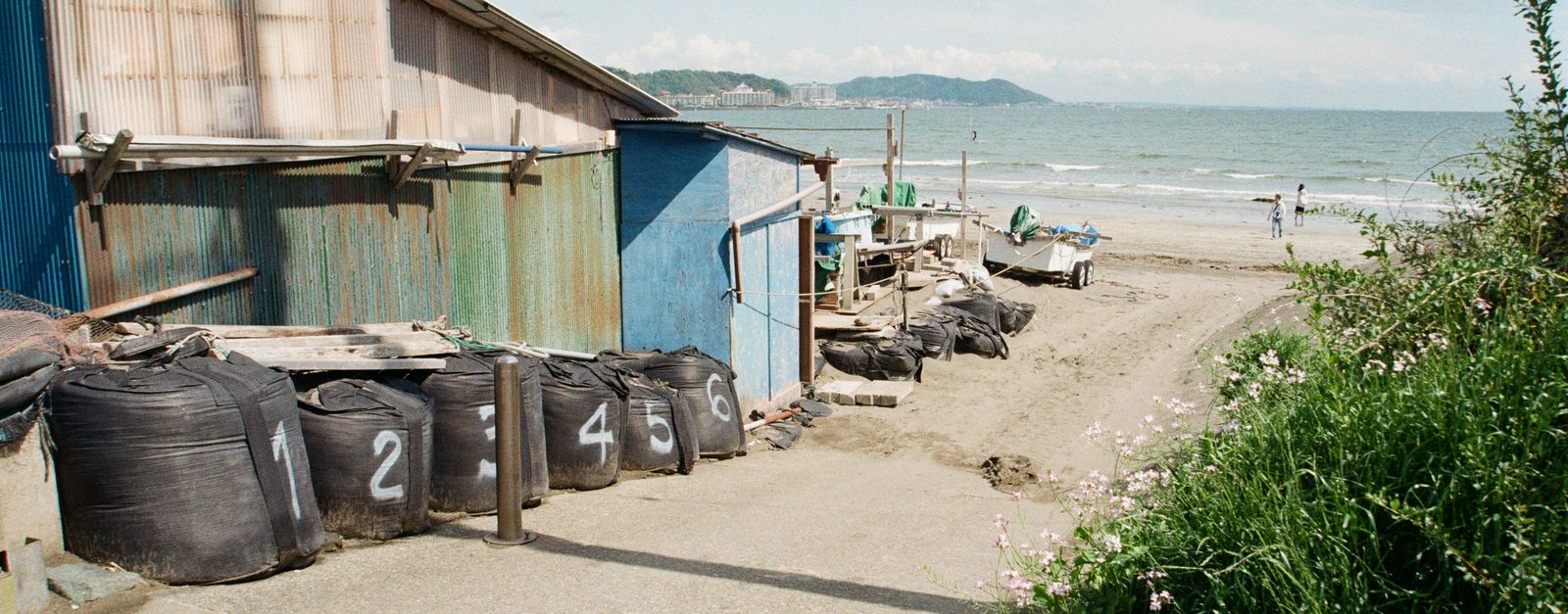 Coastal view of a rustic structure with numbered bags on Kamakura beach, Japan.