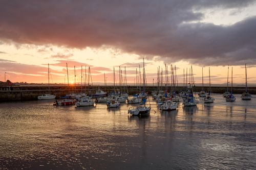 Free Tranquil view of sailboats anchored in Musselburgh Harbour as the sun sets over the Scottish coast. Stock Photo
