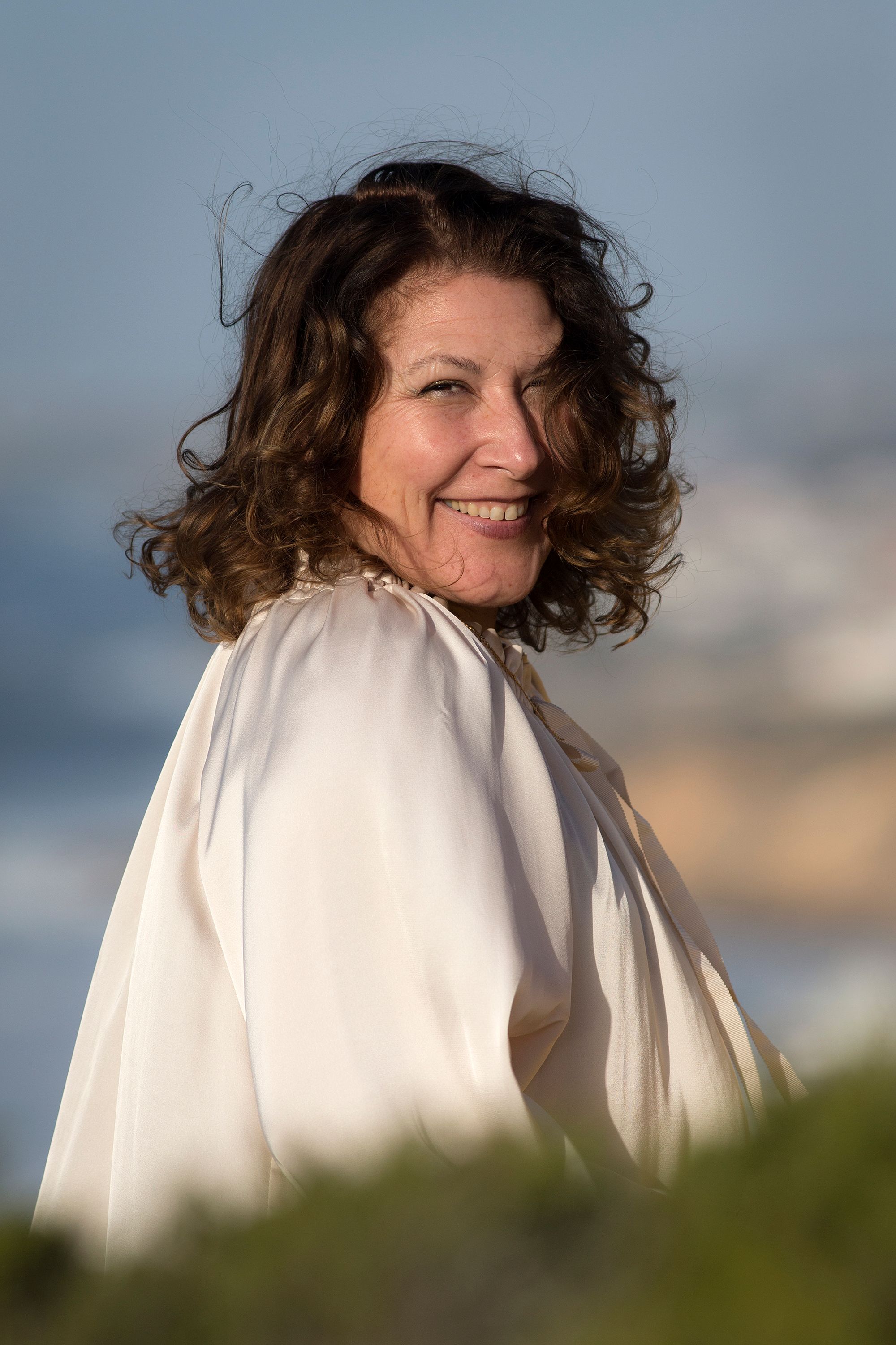 Portrait of a smiling woman enjoying the outdoors with ocean in the background under a sunny sky.