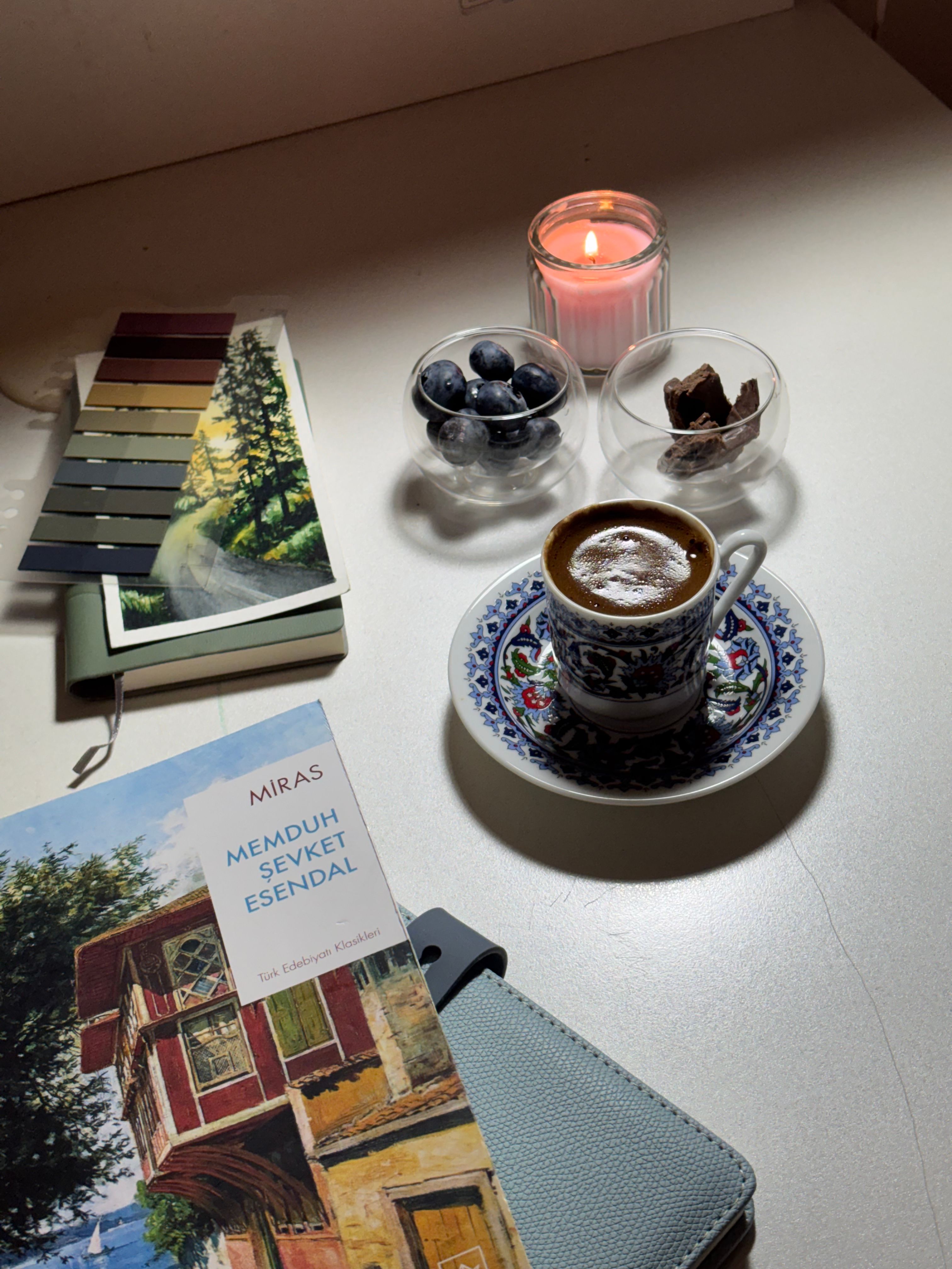 A cozy setup featuring Turkish coffee, a book, and a candle, creating a relaxing ambiance.
