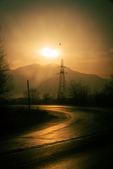 Golden sunset illuminating a winding road and silhouetted powerlines against mountains.