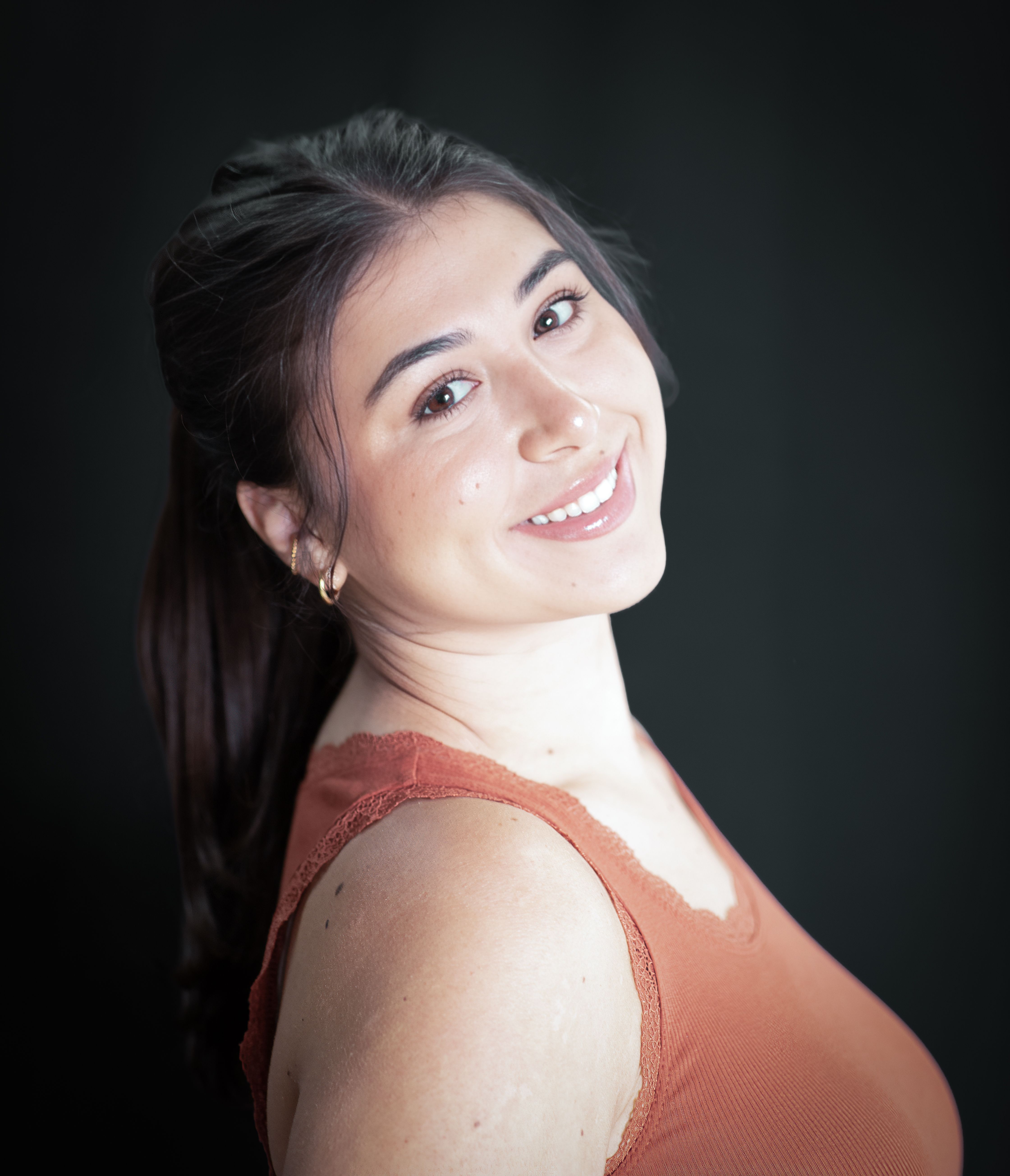 Captivating portrait of a woman smiling confidently in an orange top with a dark background.