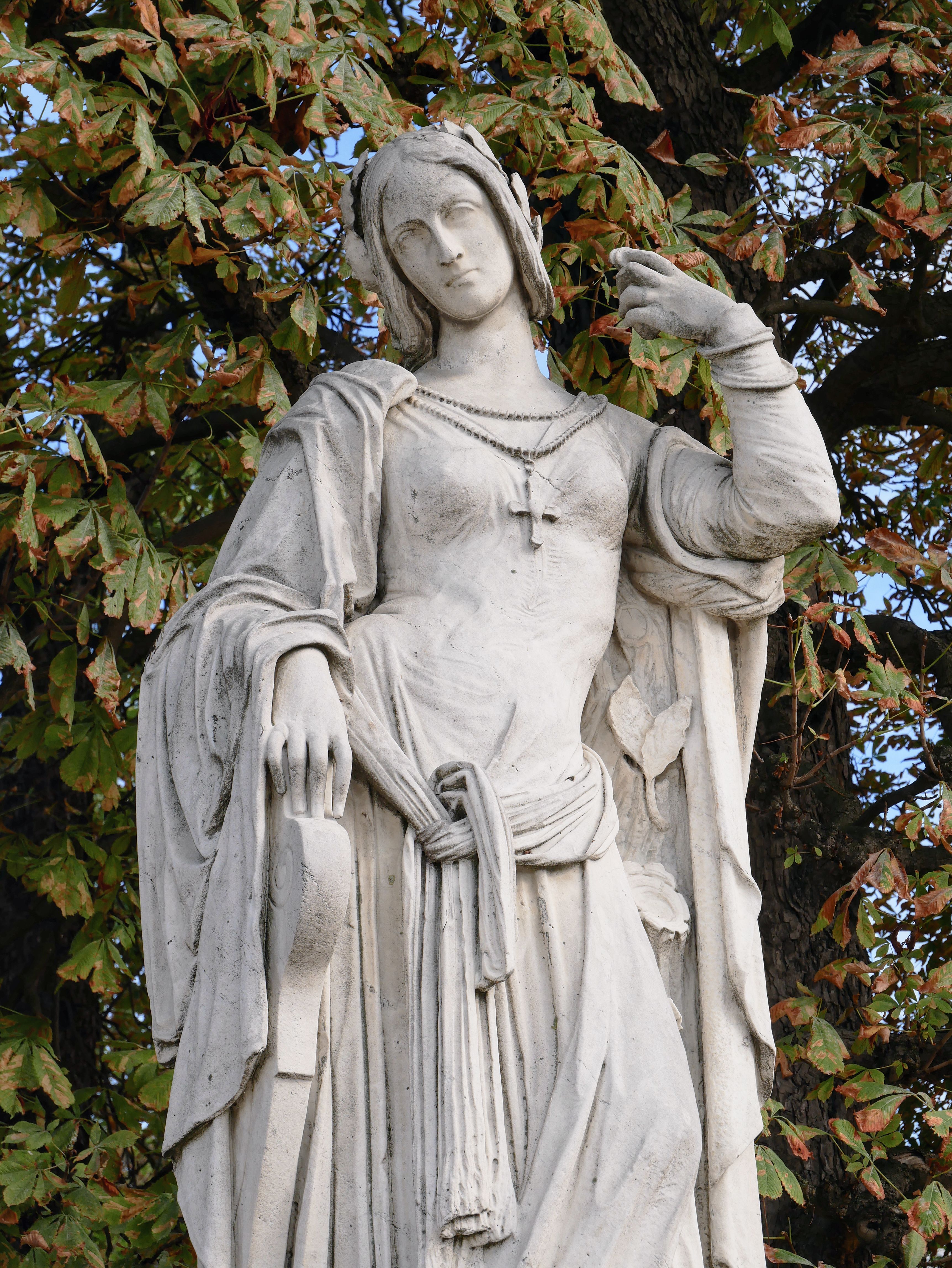 Elegant stone statue of a woman surrounded by vibrant autumn leaves, creating a serene outdoor scene.