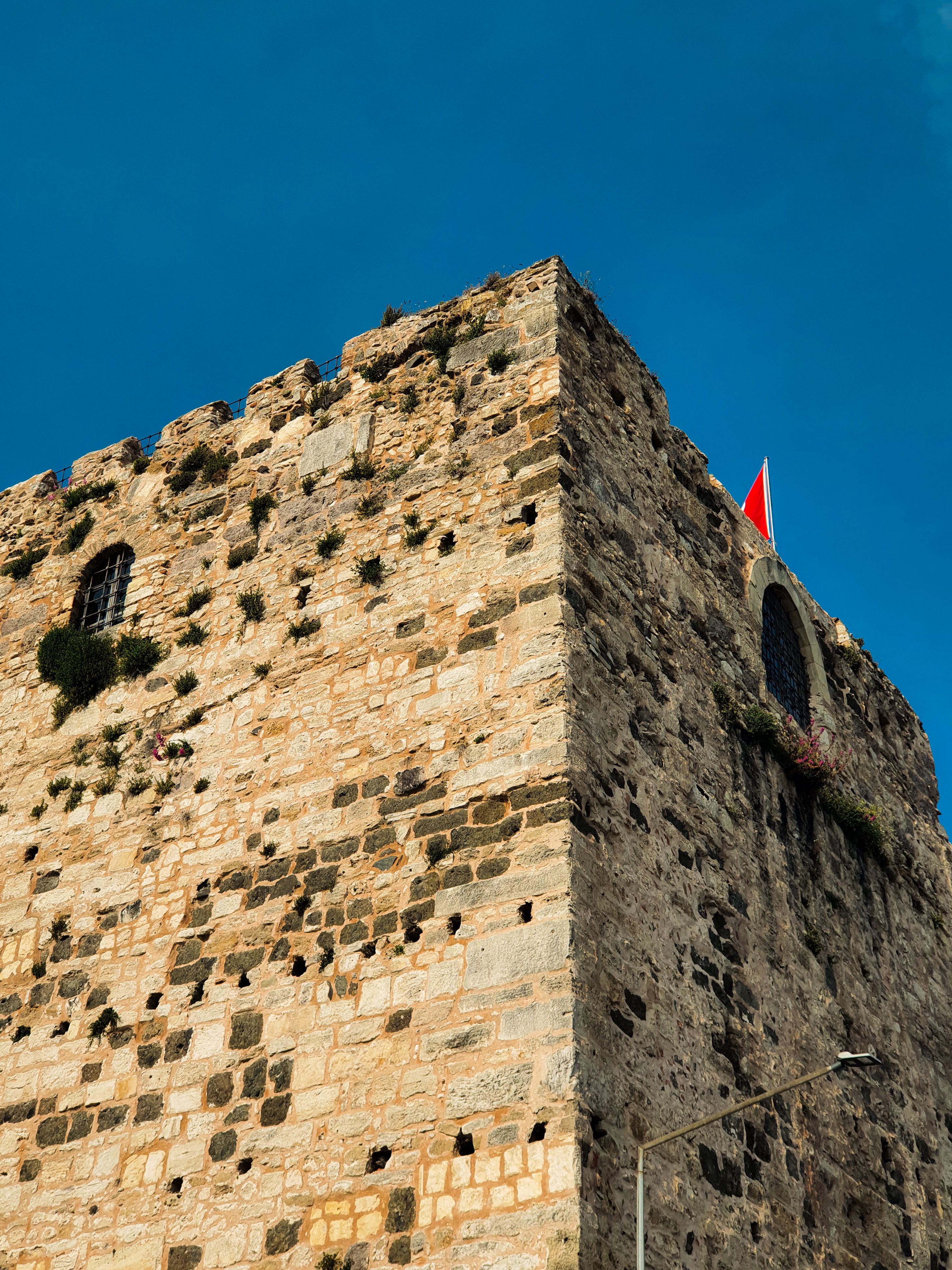 Ancient stone fortress tower against a clear blue sky with a flag, showcasing historical architecture.